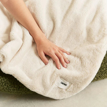 Person holding a fluffy white blanket with a visible brand label on a soft surface.