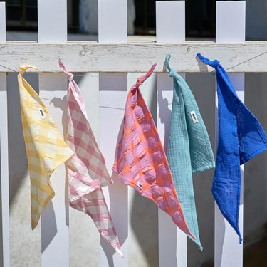 Five colorful dog bandanas hanging on a wooden rack with a neutral background